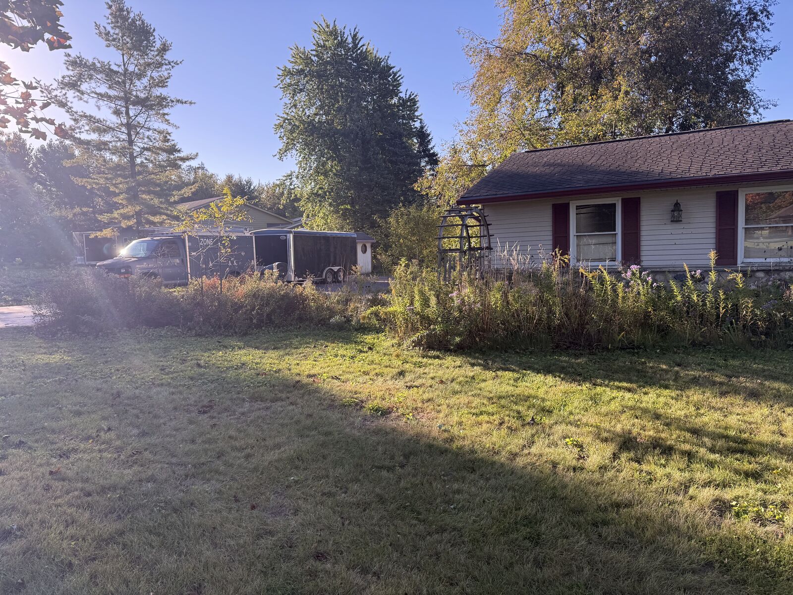 Overgrown front yard beds and weeds beside the garage, before